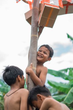 Gülen çocuklar asılma ödülüne ulaşmak için tırmanırken betel fındık tırmanma direğine tutunuyorlar.