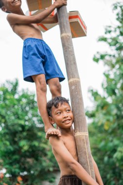 Bir çocuk, betel ceviz tırmanma yarışmasında bir arkadaşı omzunda durduğunda kolayca güler.