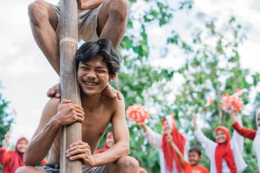 Adam Endonezya 'nın bağımsızlığını kutlamak için areca cevizine tırmanmanın ağırlığını taşırken gülüyor.