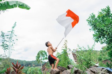 Çıplak çocuk, arkasında doğa olan Endonezya bayrağını kaldırıyor.