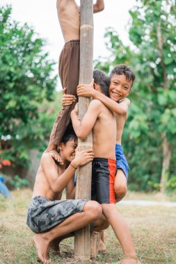 Çocuk, bağımsızlığını kutlamak için bir betel fındık tırmanma yarışmasında direğe sıkıca tutunurken gülüyor.