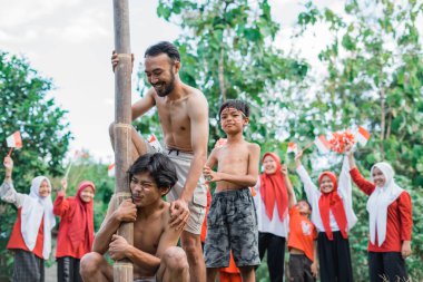 İki adam, Endonezya 'nın bağımsızlığını kutlamak için bir areca fındığına tırmanmak için birlikte çalışıyor.