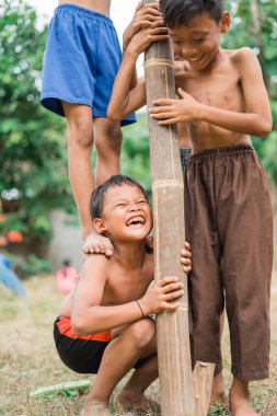 children scream to bear the weight on their shoulders during cooperation in the betel nut climbing competition clipart