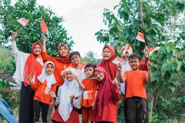 Bir grup genç kız türbanlı ve gülümseyen erkek ellerinde küçük Endonezya bayrakları tutarak bağımsızlığı kutluyorlar.