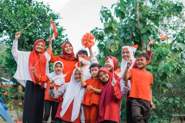 Bir grup mutlu genç kız ve oğlan birleşik bağımsızlık kutlamaları sırasında ellerinde küçük Endonezya bayrakları tutuyorlar.