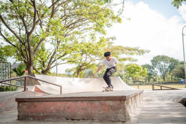 Genç bir kaykaycı açık gökyüzünün altındaki canlı bir kaykay parkında bir numara yapıyor..
