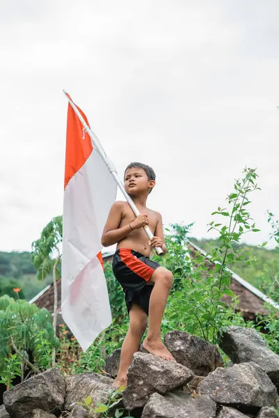 Bağımsızlık kutlamaları sırasında bir kayanın üzerinde duran Endonezya bayrağı taşıyan üstsüz Cava 'lı çocuk.