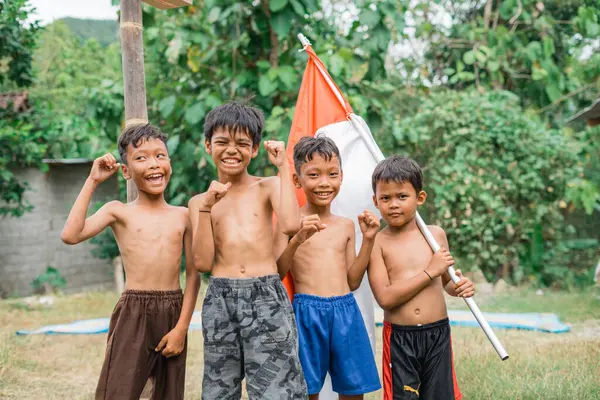Dört heyecanlı Cava çocuğu, bağımsızlık kutlamaları sırasında bir Endonezya bayrağı taşırken kameraya bakıyorlar.