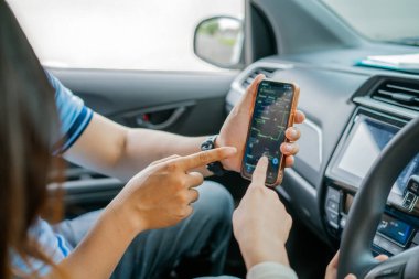 İki kişi, bir aracın içindeyken navigasyon için bir akıllı telefonu yakından inceliyor.