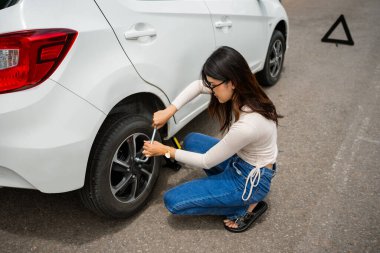 Bir kadın açık havada ve aktifken aracının patlak lastiğini güvenle tamir eder.
