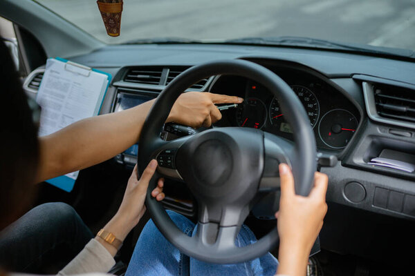 A driving instructor points at the dashboard, aiding student in steering lessons.