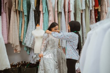 İki genç kız neşeyle kumaşlarla dolu canlı bir butikte zarif elbiseler keşfediyor.