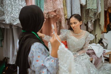 Güzel bir gelin göz kamaştırıcı bir elbise denerken stilistinden uzman rehberliği alıyor.