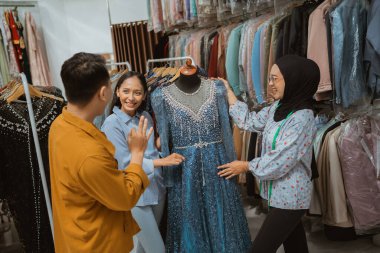 Üç yakın arkadaş bir butik dükkanında büyüleyici derecede güzel mavi bir elbiseye bakıp hayranlık duyuyorlar.