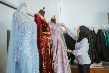 Tasarımcı ince giyimli ve bir butikte göz kamaştırıcı gece elbiseleri tasarlıyor, zarafeti vurguluyor.