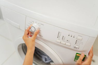 Eller, modern bir çamaşır makinesinin kadranını dikkatlice ayarlıyor.