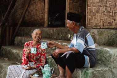 Yaşlı bir çift, mutluluklarını yansıtan geleneksel bir ortamda çay ve kahkahayı sever.