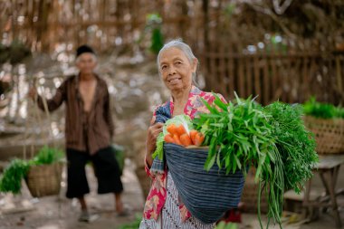 Yaşlı bir kadın canlı bir pazarda neşeyle parıldıyor, elinde taze sebzelerle dolu bir sepet tutuyor.