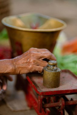 Yaşlı bir el, bir dizi taze ürünle çevrili vintage bir ölçek üzerinde küçük bir ağırlığı dikkatle dengeler