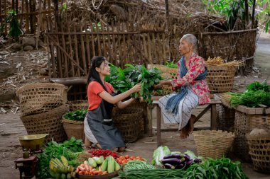 Canlı ve renkli bir piyasa sahnesinde iki kadın canlı taze ürün alışverişi yapıyor.
