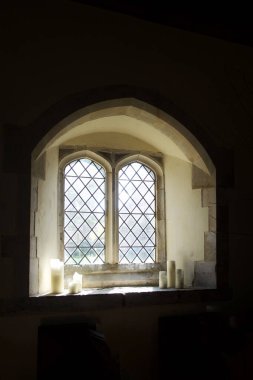   Pencerenin pervazında, pencerenin pervazında ve altında üç beyaz mum bulunan bir kilise penceresinden ışık yayılıyor. Duvarlar siyah, kopyalama alanı için ideal, Ringmer Kilisesi, Ringmer, Doğu Sussex, Birleşik Krallık