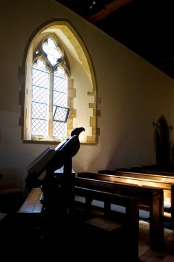  Kilise içi, iki kemerli kilise penceresinden akan ışık, pencerenin önünde üzerinde İncil olan kilise sıraları var. Ön planda bir kartal şekilli ahşap kürsü var. Işık dramatik bir şekilde gotik bir atmosfer yaratıyor.