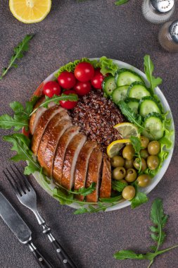 Fırında tavuk göğsü, kinoa, vişneli domates, salatalık, zeytin, marul yaprağı ve roka kahverengi masada.