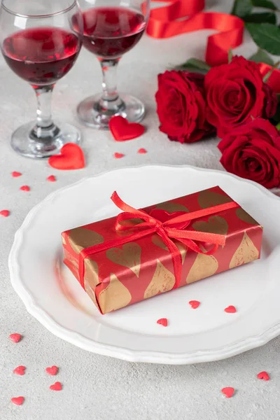 情人节的概念 白盘纸包礼物 红玫瑰和两杯玻璃杯酒放在茶几上 — 图库照片