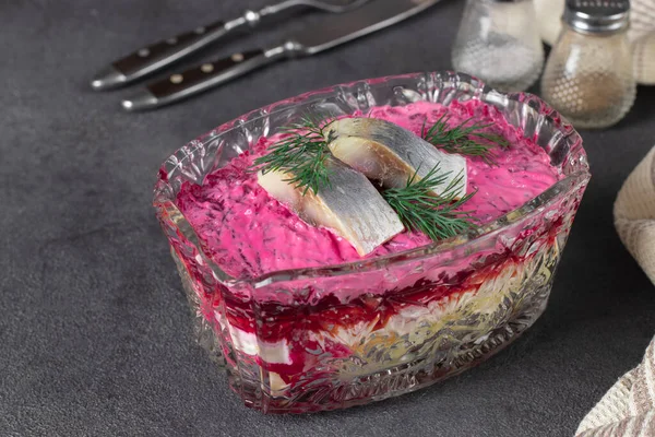 俄罗斯传统假日沙拉鲱鱼皮大衣下的透明色拉碗灰色背景 — 图库照片