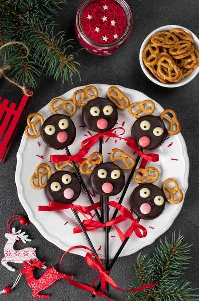 Cake pops Santa\'s reindeers made from cookies in chocolate and crackers on white plate, Top view