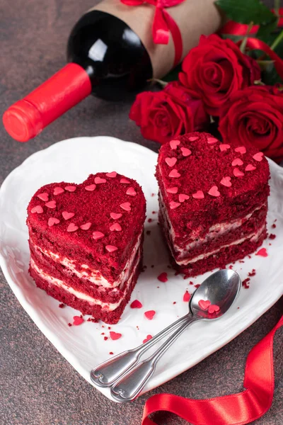 在白色的盘子里 红绒心形的蛋糕 在棕色的背景上 为情人节准备的玫瑰和葡萄酒 垂直的图像 — 图库照片