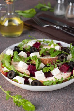 Pancar, tavuk, peynir, roka ve kahverengi arkaplanda siyah zeytinli salata.