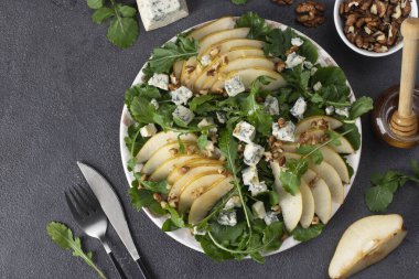 Salata roka, armut, mavi peynir, bal ve ceviz gri masada.