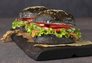 İki vejetaryen siyah burger, tuzlanmış somon, yengeç eti ve sebzeler tahtada kahverengi arka planda.