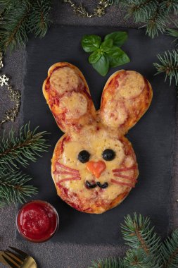 Domates soslu, salamlı, peynirli, siyah zeytinli ve fesleğenli tatlı tavşanlı pizza. Yeni yıl için yemek fikri 2023, Top view