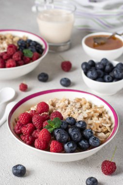 Yulaf ezmeli yulaf lapası, yabanmersini, ahududu ve açık gri arka planda bal. Kahvaltı yemeği konsepti, dikey görüntü