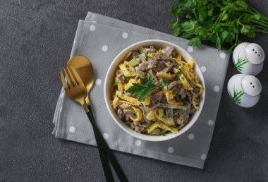 Tavuk mideli salata, çırpılmış krep ve kızarmış soğan gri arka planda beyaz bir kasede.