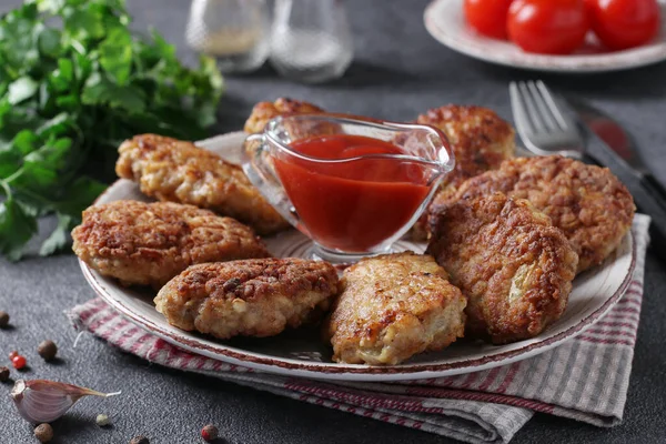 Cutlets of turkey fillet and oatmeal, fried in a pan, served with tomato sauce on gray table