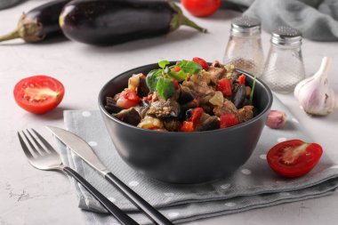 Meat stew with eggplant and tomatoes served in dark bowl on gray background