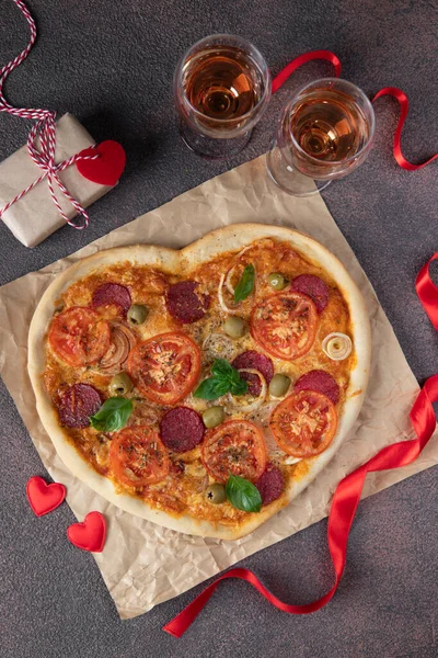 Heart shaped pizza with tomatoes, salami sausage and cheese for Valentines Day on brown background, Top view, Vertical image