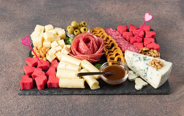 Charcuterie board for Valentines Day with varieties sausage, cheese, nuts, olives and cheese dip fig