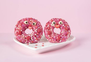Donuts with bright pink glaze in heart-shaped plate on pink background, Food concept of romantic love