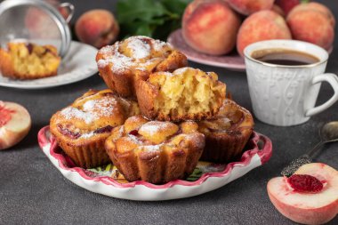 Homemade muffins with peaches sprinkled powdered sugar on plate on gray background