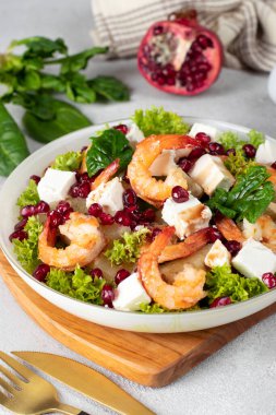 Salad with shrimps, pineapple, feta and pomegranate seeds in plate on green lettuce leaves, on wooden board, Vertical format