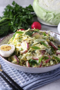 Salad with cabbage, radishes, parsley, green onions and eggs, seasoned with sour cream on gray background. Healthy food