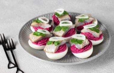 Eggs stuffed with beets and salted herring, garnished with parsley and onion on light gray background
