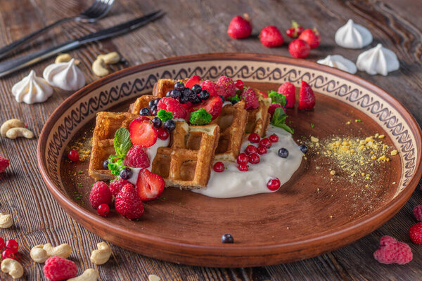 Belgian waffles on breakfast with berries, nuts and cream cheese in a plate on wooden table