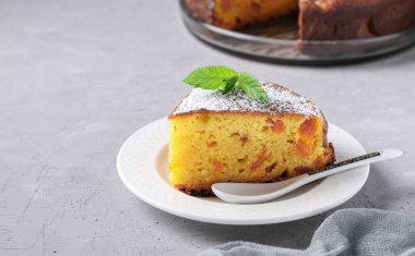 Ön planda bir parça kesilmiş kurutulmuş kayısılı ev yapımı peynirli turta, gri arka plan.