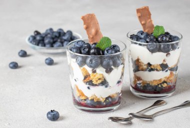 Açık gri arka planda bisküvi, yaban mersini, krema ve çikolatalı tatlı.