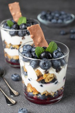 Koyu gri arka planda gözlüklü, yaban mersinli, kremalı ve çikolatalı tatlı, dikey format